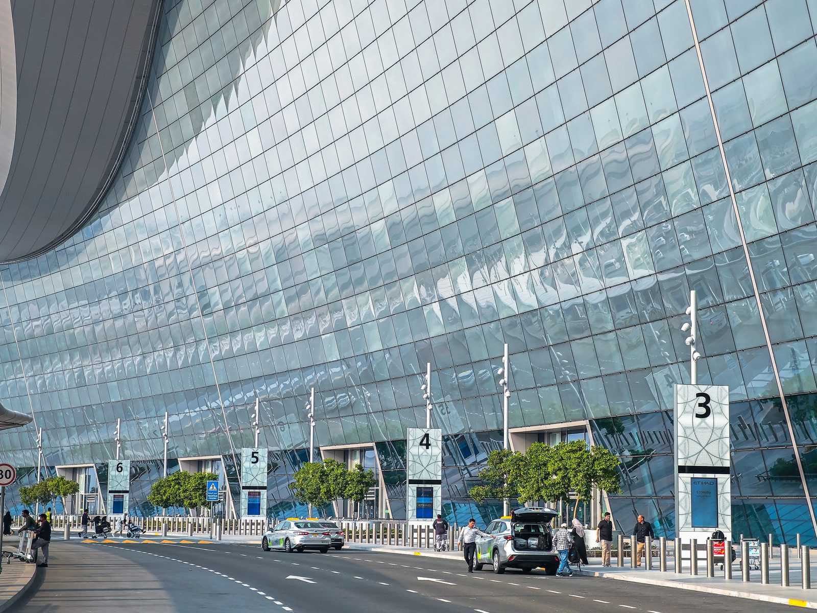 Modern glass façade of Zayed International Airport Terminal A in Abu Dhabi, photographed from the arrival approach